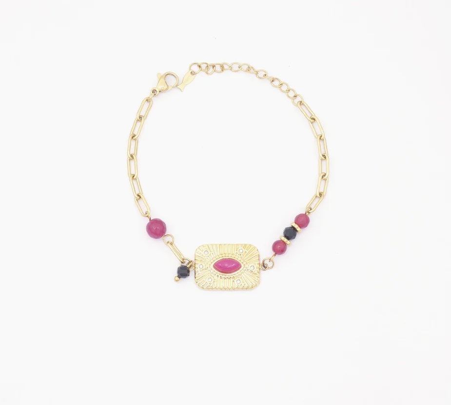 Ce bracelet maille urbaine, en acier inoxydable et plaqué or, se distingue par son design audacieux et élégant. Au centre, un rectangle en plaqué or aux angles arrondis abrite une pierre rose, entourée de gravures rayonnantes évoquant un soleil ou un œil mystique. De chaque côté de ce rectangle, la chaîne est ornée de perles roses et noires : une seule perle rose d'un côté, et deux perles roses et une perle noire de l'autre.