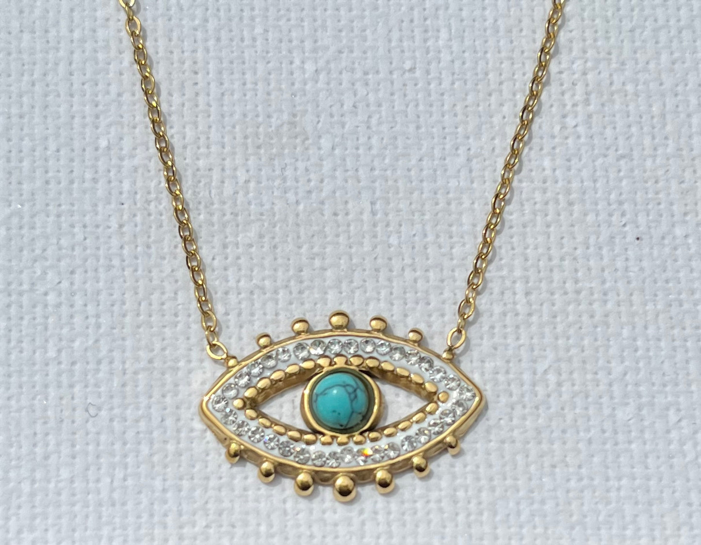 Découvre notre collier multi-chaînes, en acier inoxydable et plaqué or. Ce bijou se compose de trois chaînes, chacune apportant sa touche unique. La première chaîne est une élégante maille chevron, ornée d'une perle turquoise. La seconde chaîne, plus courte, présente des maillons ovales entrelacés, créant un jeu de textures. Enfin, la troisième chaîne, plus fine et minimaliste, met en avant un pendentif en forme d’œil, serti de zircons et d'une pierre turquoise centrale.