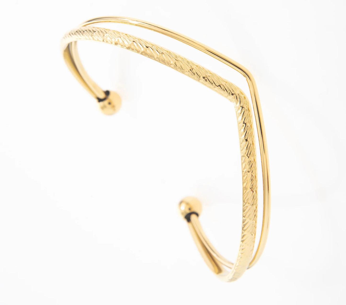 Jonc Zélie en acier inoxydable et plaqué or. Le bracelet se distingue par sa forme en pointe arrondie au centre, dirigée vers la main. Il est composé de deux branches distinctes : la première est fine et minimaliste, tandis que la seconde, légèrement plus épaisse et subtilement espacée, est ornée de gravures en traits très fins, ajoutant une texture délicate. Les deux branches sont maintenues à leurs extrémités par de petites boules élégantes de chaque côté,