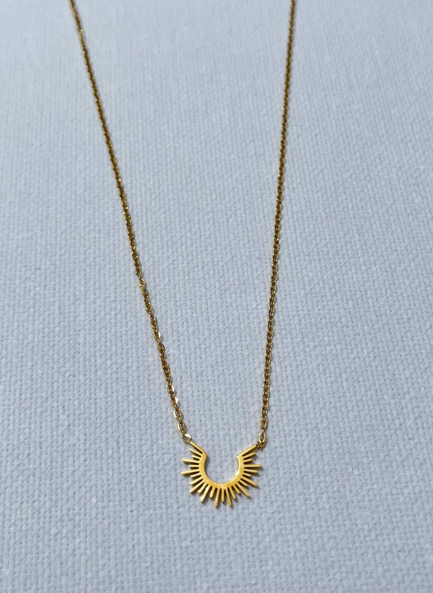 Découvre notre collier au charme solaire, en acier inoxydable et plaqué or. Ce bijou fin est composé d'une chaîne de type forçat. Son pendentif en forme de demi-soleil apporte une touche de lumière à ton décolleté. Chic, minimaliste et facile à porter, ce collier est le must-have pour toutes les femmes qui aiment se démarquer tout en restant élégantes. Craque pour ce bijou qui fera rayonner ton style.