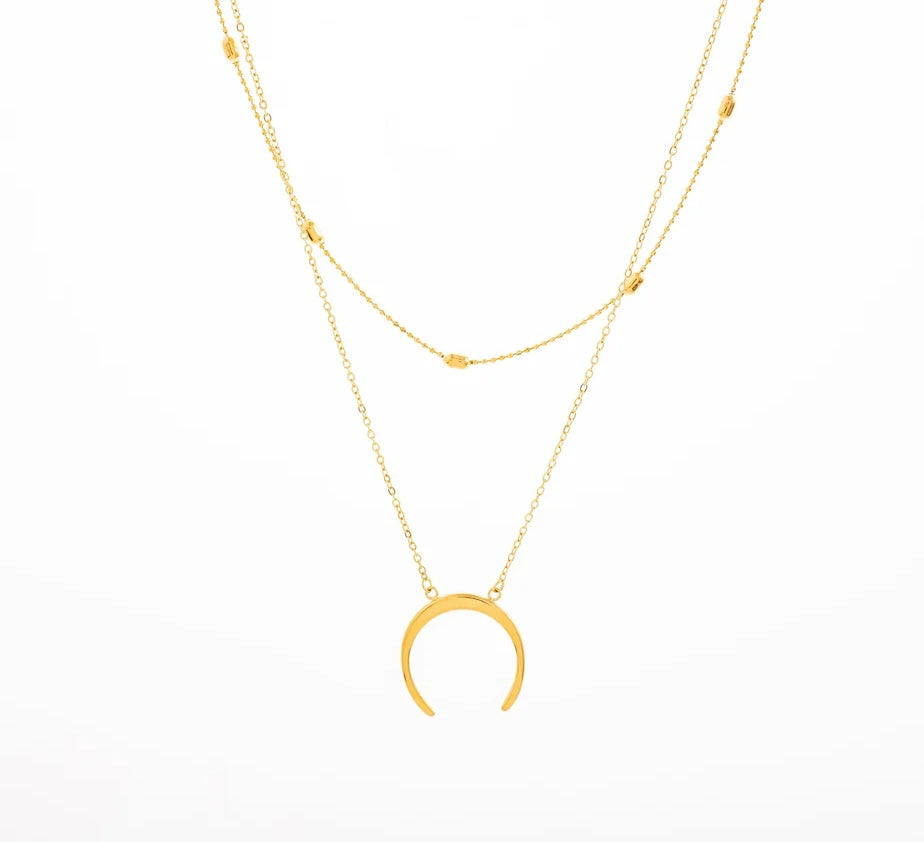 Ajoute une touche bohème à ton look avec ce superbe collier double rang, en acier inoxydable et plaqué or. Sa première chaîne est en maille forçat ornée de petites perles dorées, tandis que la seconde met en valeur un pendentif en croissant de lune, symbole de féminité et de renouveau. Porte-le seul pour un effet chic minimaliste ou superpose-le avec d'autres colliers pour un look plus audacieux.

