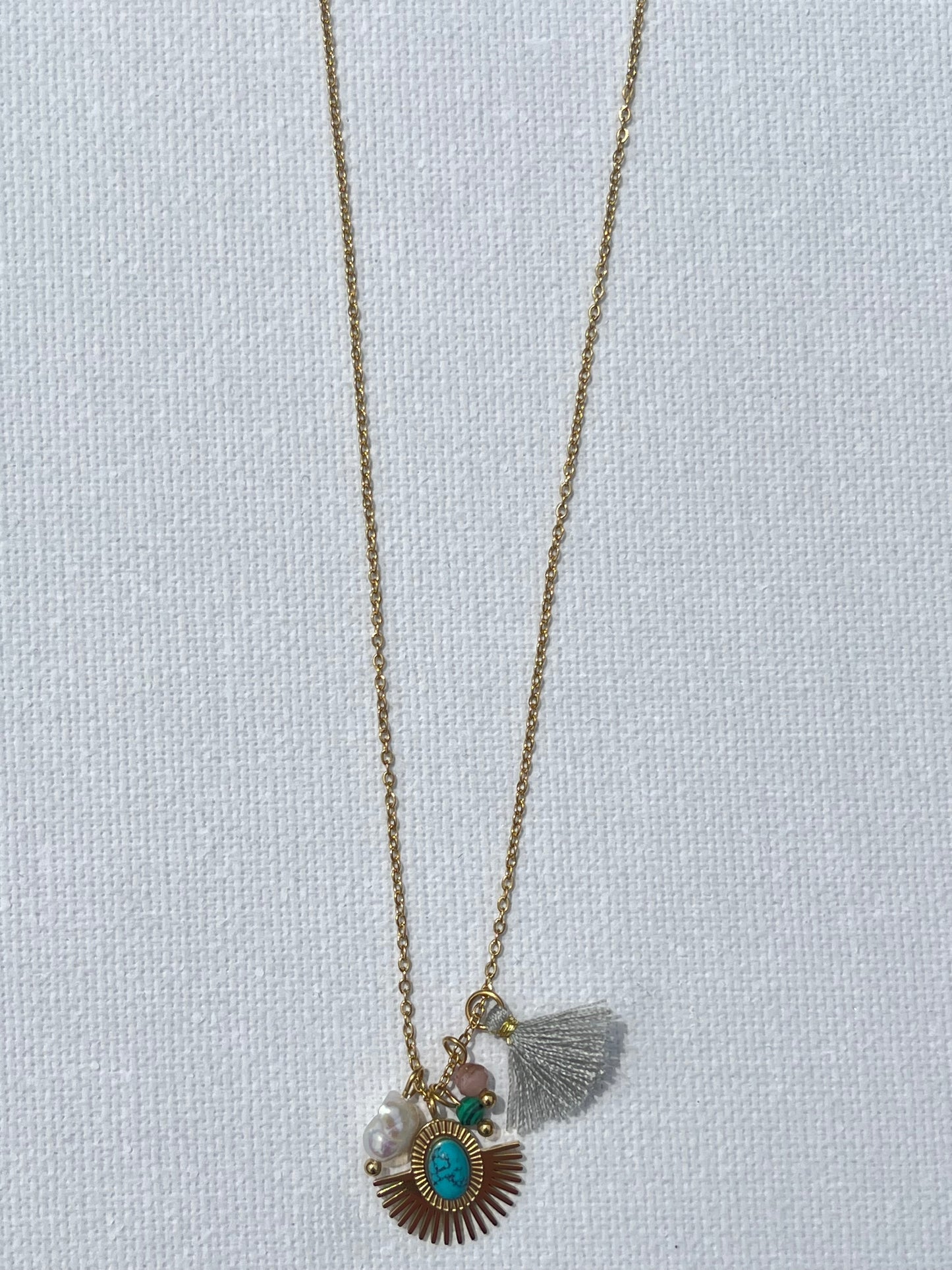 Opte pour ce collier, en acier inoxydable et plaqué or, parfait pour sublimer tes tenues. Sa chaîne fine en maille forçat met en valeur un pendentif médaillon solaire, rehaussé d'une pierre turquoise au centre, symbole de protection et de sérénité. Il est accompagné d'une perle nacrée, d'une pierre rose pâle et d’un pompon gris délicat. Ce collier polyvalent se marie aussi bien avec un look décontracté qu’avec une tenue plus sophistiquée.