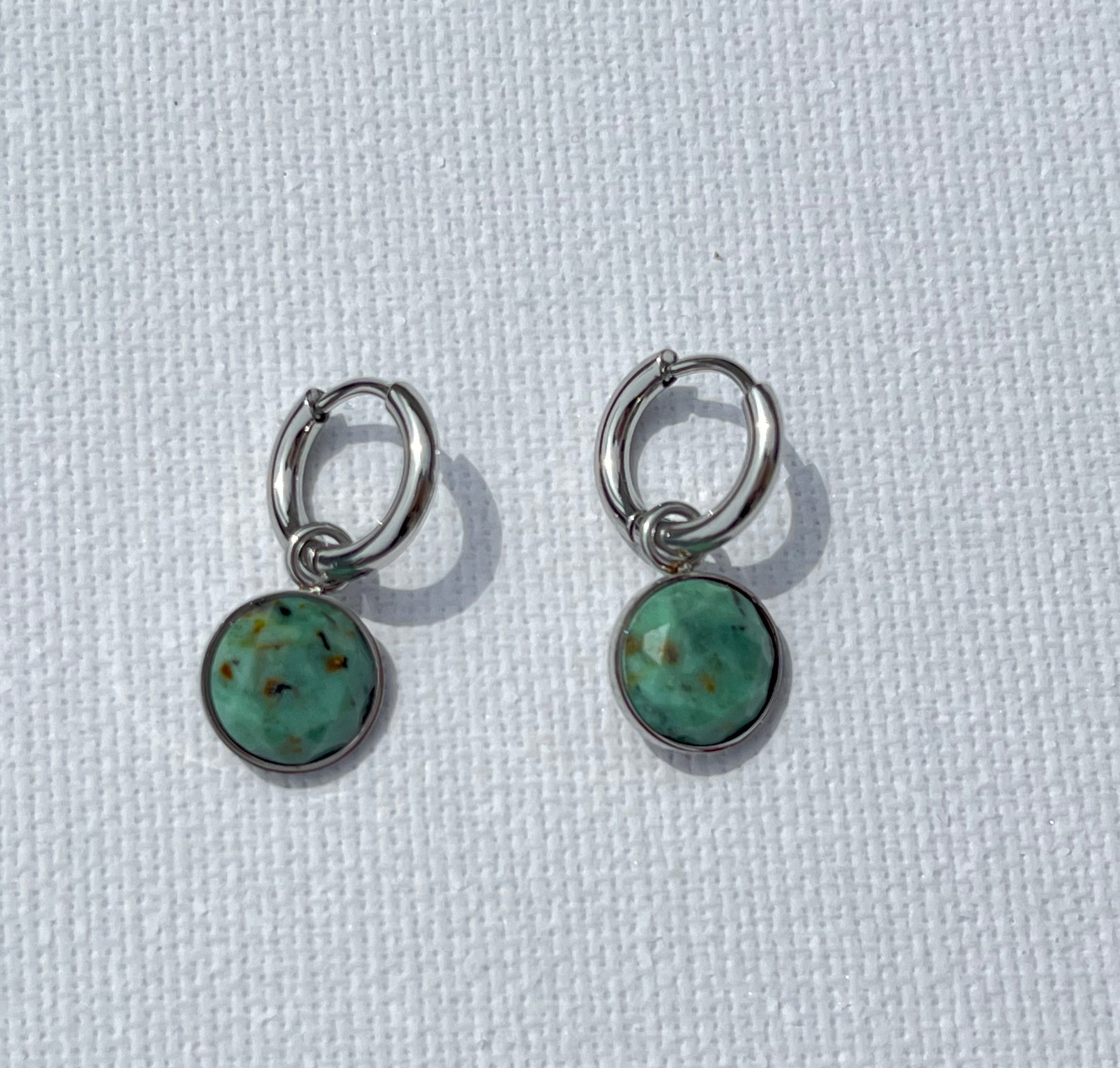 Succombe au charme de ces boucles d'oreilles, en acier inoxydable et argent, un subtil mélange entre simplicité et caractère. Ces créoles en argent, agrémentées d’un pendentif rond en pierre naturelle, apportent une touche de fraîcheur et d'authenticité à ton style. Les variations délicates de vert et de brun dans la pierre créent un effet unique.