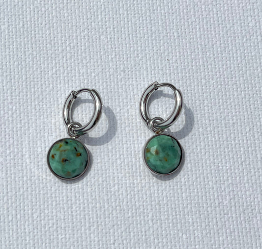 Succombe au charme de ces boucles d'oreilles, en acier inoxydable et argent, un subtil mélange entre simplicité et caractère. Ces créoles en argent, agrémentées d’un pendentif rond en pierre naturelle, apportent une touche de fraîcheur et d'authenticité à ton style. Les variations délicates de vert et de brun dans la pierre créent un effet unique.