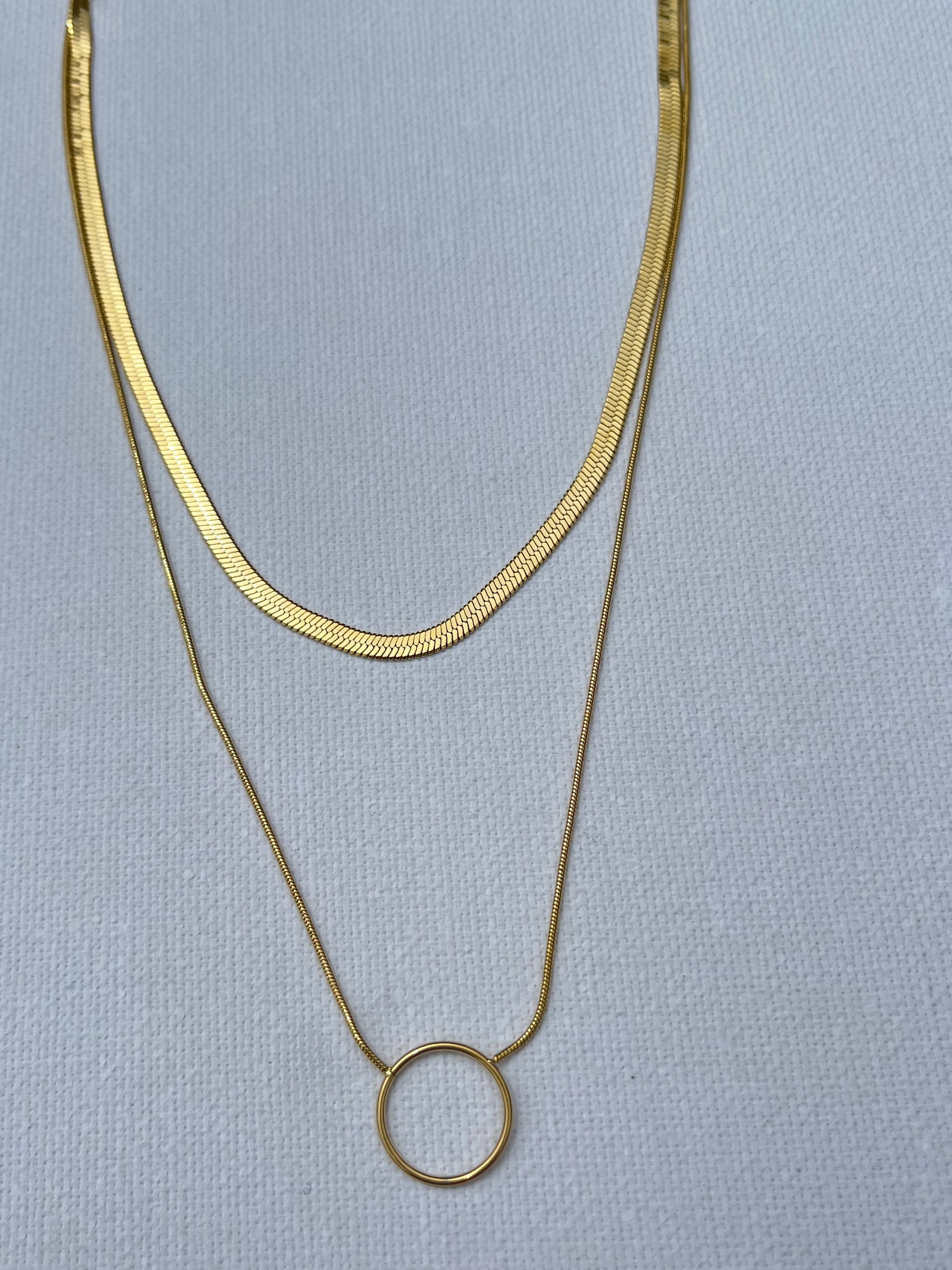 Succombe au charme de ce collier double, en acier inoxydable et plaqué or, parfait pour apporter une touche d'élégance à toutes tes tenues. La première chaîne, délicate et épurée, se distingue par sa maille miroir simple qui capte la lumière à chaque mouvement. La seconde chaîne, plus audacieuse avec sa maille serpent, est sublimée par un anneau central en plaqué or. Ce duo chic et minimaliste se marie parfaitement pour créer un look moderne et intemporel.