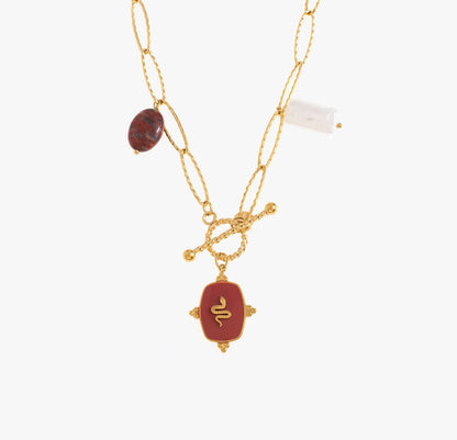 Un collier, en acier inoxydable et plaqué or, qui sort du lot. La chaîne épaisse en mailles ovales et les pierres naturelles apportent une touche d’authenticité : jaspe, quartz, et ce pendentif rouge profond orné d’un serpent doré, symbole de puissance et de transformation. Le fermoir T qui se ferme à l’avant, ajoute une touche stylée et pratique. Un bijou audacieux, pour une femme audacieuse.