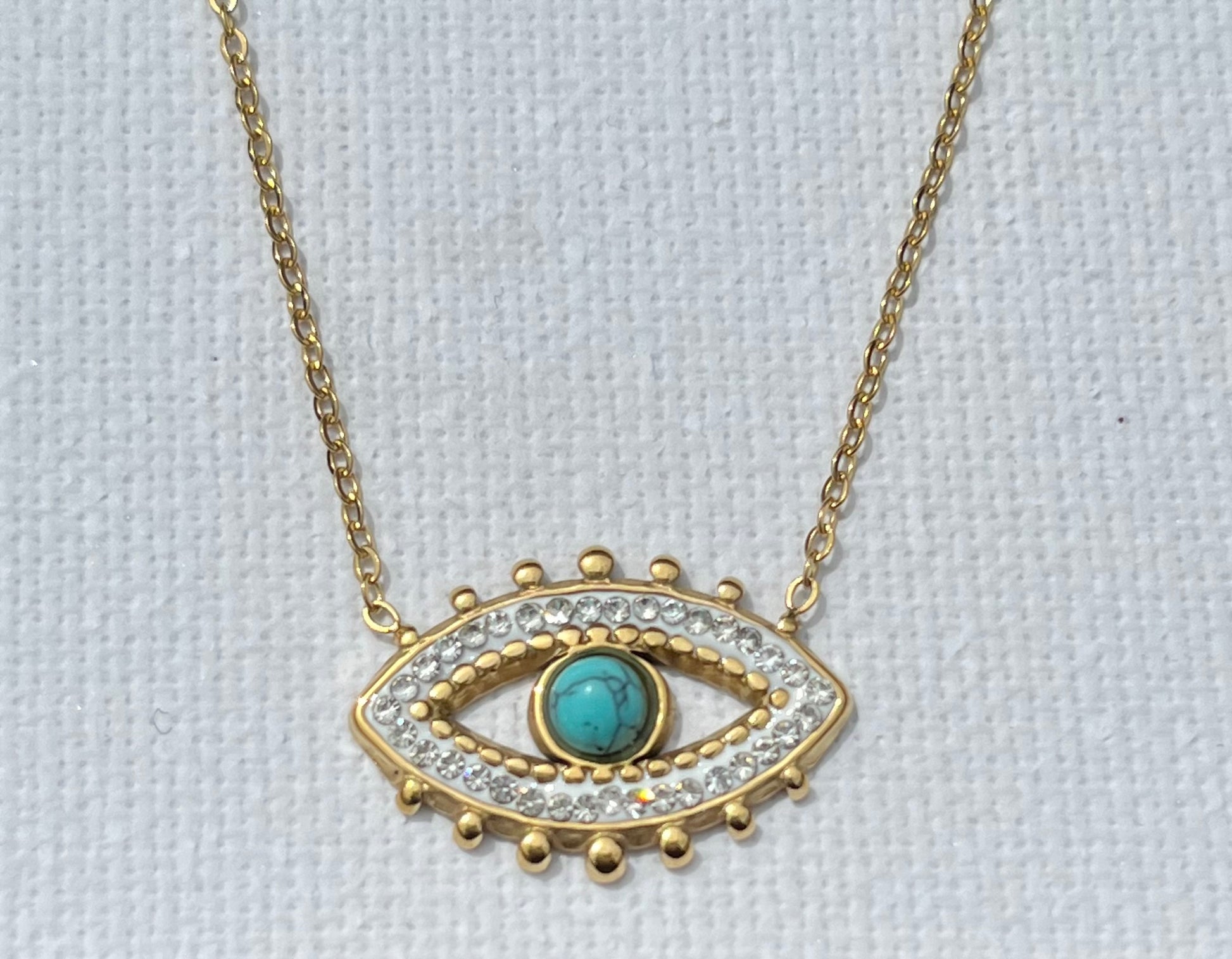 Découvre notre collier multi-chaînes, en acier inoxydable et plaqué or. Ce bijou se compose de trois chaînes, chacune apportant sa touche unique. La première chaîne est une élégante maille chevron, ornée d'une perle turquoise. La seconde chaîne, plus courte, présente des maillons ovales entrelacés, créant un jeu de textures. Enfin, la troisième chaîne, plus fine et minimaliste, met en avant un pendentif en forme d’œil, serti de zircons et d'une pierre turquoise centrale.