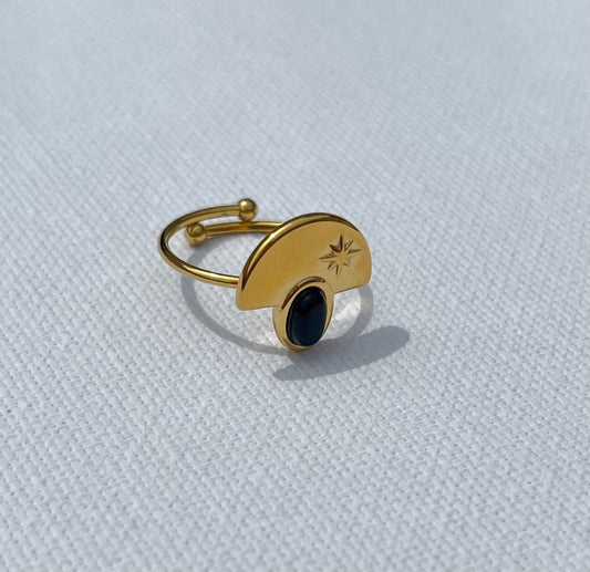 Découvre notre bague demi-lune, en acier inoxydable et plaqué or. Cette bague unique affiche une pierre noire en cabochon, parfaitement nichée sous une plaque dorée gravée d'une étoile. Le contraste saisissant entre l'éclat doré et la profondeur de la pierre noire apportera une dimension chic à toutes tes tenues. Ajustable et confortable, ce bijou est parfait si tu veux allier sophistication et originalité. 