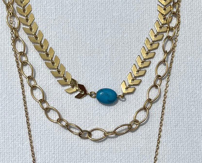 Découvre notre collier multi-chaînes, en acier inoxydable et plaqué or. Ce bijou se compose de trois chaînes, chacune apportant sa touche unique. La première chaîne est une élégante maille chevron, ornée d'une perle turquoise. La seconde chaîne, plus courte, présente des maillons ovales entrelacés, créant un jeu de textures. Enfin, la troisième chaîne, plus fine et minimaliste, met en avant un pendentif en forme d’œil, serti de zircons et d'une pierre turquoise centrale.