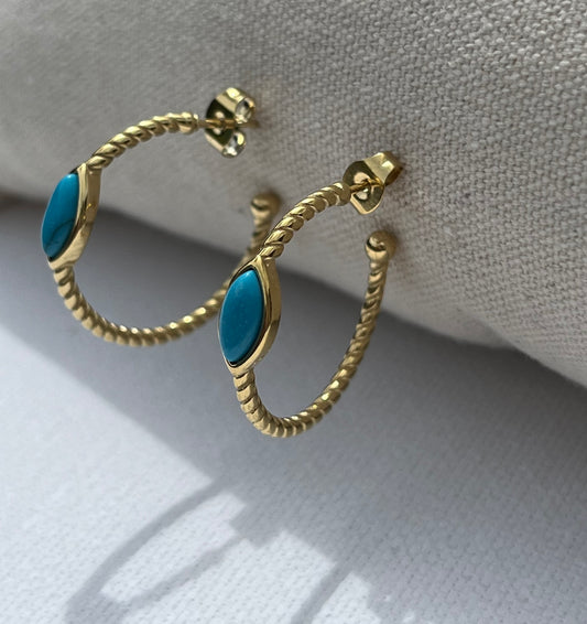 Ces créoles, en acier inoxydable et plaqué or, à la torsade élégante, ornées d'une pierre turquoise en forme d'amande, sont l'accessoire parfait pour apporter une touche d'exotisme à ton look. Le contraste subtil entre l'or et la turquoise crée un équilibre chic et lumineux, idéal pour illuminer tes tenues d'été ou ajouter un twist original à ton style quotidien.


