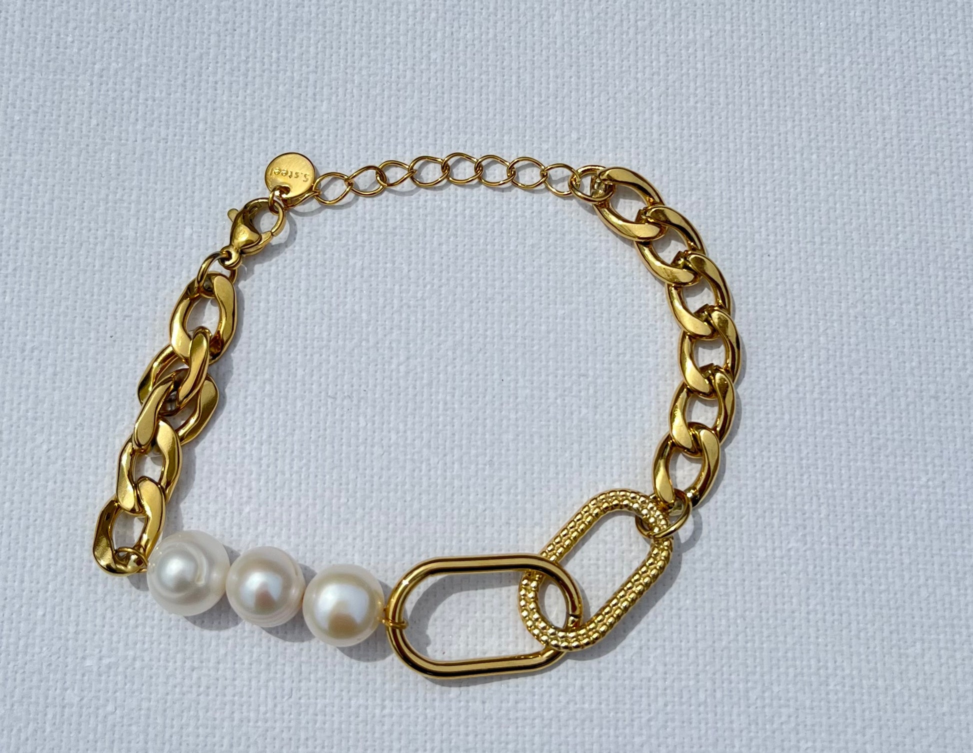 Ce bracelet en maille gourmette se distingue par son design unique et raffiné. Au centre, trois véritables perles d'eau douce apportent une touche d'élégance naturelle et deux ovales en plaqué or entrelacés, dont l'un est délicatement gravé de motifs en point. Un bijou sophistiqué et moderne, parfait pour rehausser n'importe quelle tenue avec une note d'élégance intemporelle.