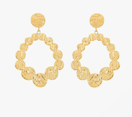 Ces boucles d'oreilles, en acier inoxydable et plaqué or, sont faites pour celles qui osent affirmer leur style. Inspirées des formes organiques et des textures martelées. Composées de larges cercles irréguliers. Leurs motifs circulaires imbriqués forment un ovale original. La partie supérieure est un bouton rond également texturé. Ces boucles d'oreilles incarnent la féminité : fortes, audacieuses, et lumineuses. Associe-les à des cheveux relevés pour un effet maximal !