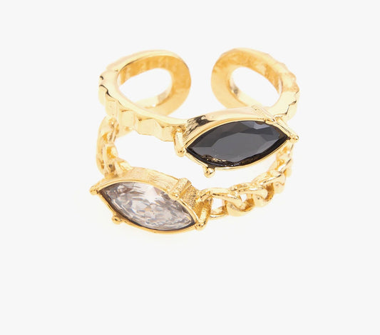 Sublime ton style avec cette bague en acier inoxydable, plaqué or, composée de deux anneaux délicatement reliés. Chaque anneau est orné d'un cristal en forme de marquise, l'un noir profond et l'autre transparent, créant un contraste saisissant et raffiné. La texture martelée des anneaux et les détails en chaîne apportent une touche moderne à ce design chic. Cette bague est également réglable, s'adaptant parfaitement à ton doigt.
