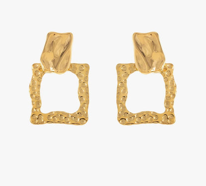 Découvre ces boucles d'oreilles élégantes, en acier inoxydable et plaqué or. Elles arborent une forme géométrique avec un design texturé. La partie supérieure est subtilement sculptée, évoquant un effet martelé, tandis que la base présente un carré ouvert aux bords irréguliers, créant un contraste visuel. Léger et confortable, ce bijou se porte facilement au quotidien. Adopte ce bijou unique pour ajouter une pointe d'originalité à ton look.