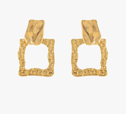 Découvre ces boucles d'oreilles élégantes, en acier inoxydable et plaqué or. Elles arborent une forme géométrique avec un design texturé. La partie supérieure est subtilement sculptée, évoquant un effet martelé, tandis que la base présente un carré ouvert aux bords irréguliers, créant un contraste visuel. Léger et confortable, ce bijou se porte facilement au quotidien. Adopte ce bijou unique pour ajouter une pointe d'originalité à ton look.